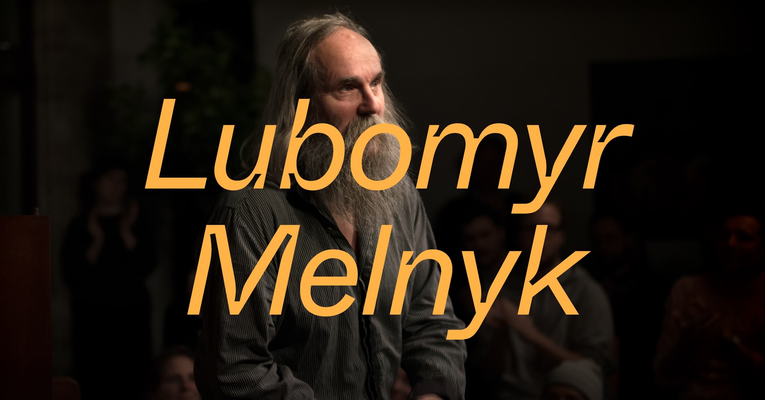 An old man with long hair and a beard stands in a dimly lit room, with the text "Lubomyr Melnyk" overlaid in large letters.