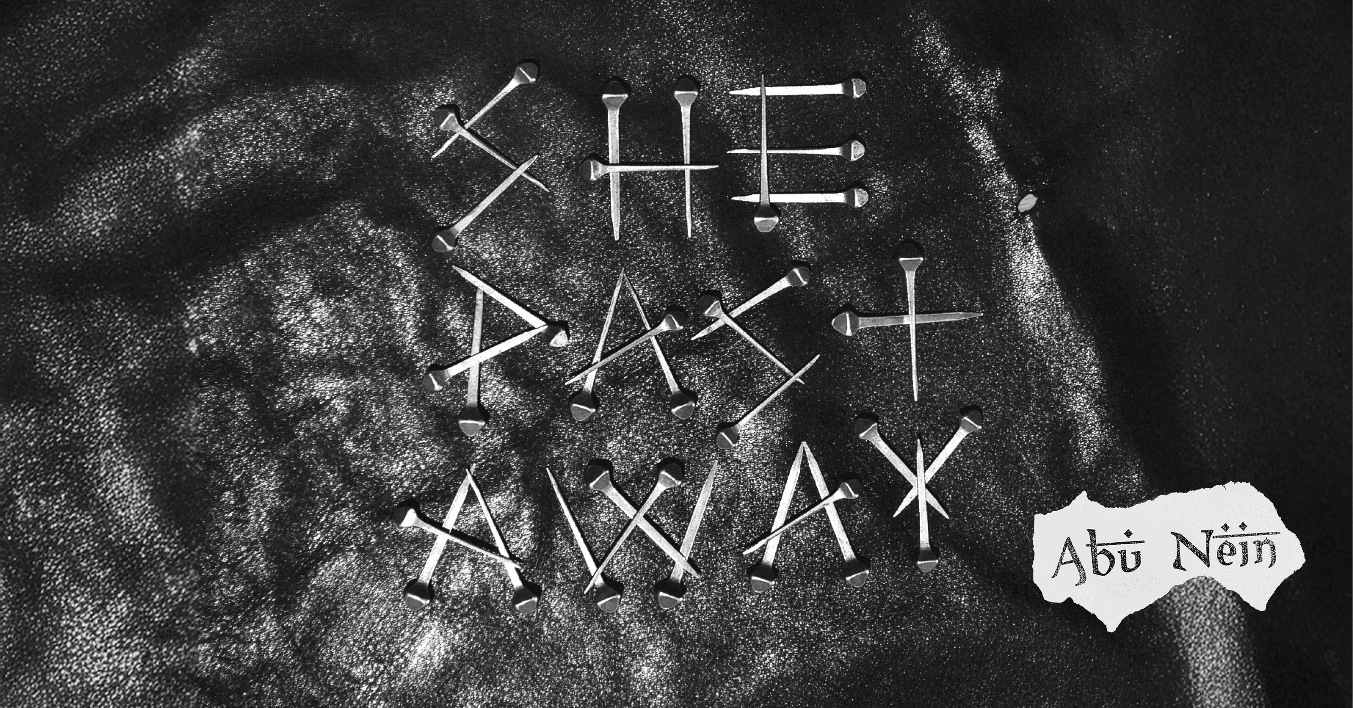 The words "She Past Away" are spelled out with nails on a textured black surface, with "Abu Nein" written on a torn piece of paper.