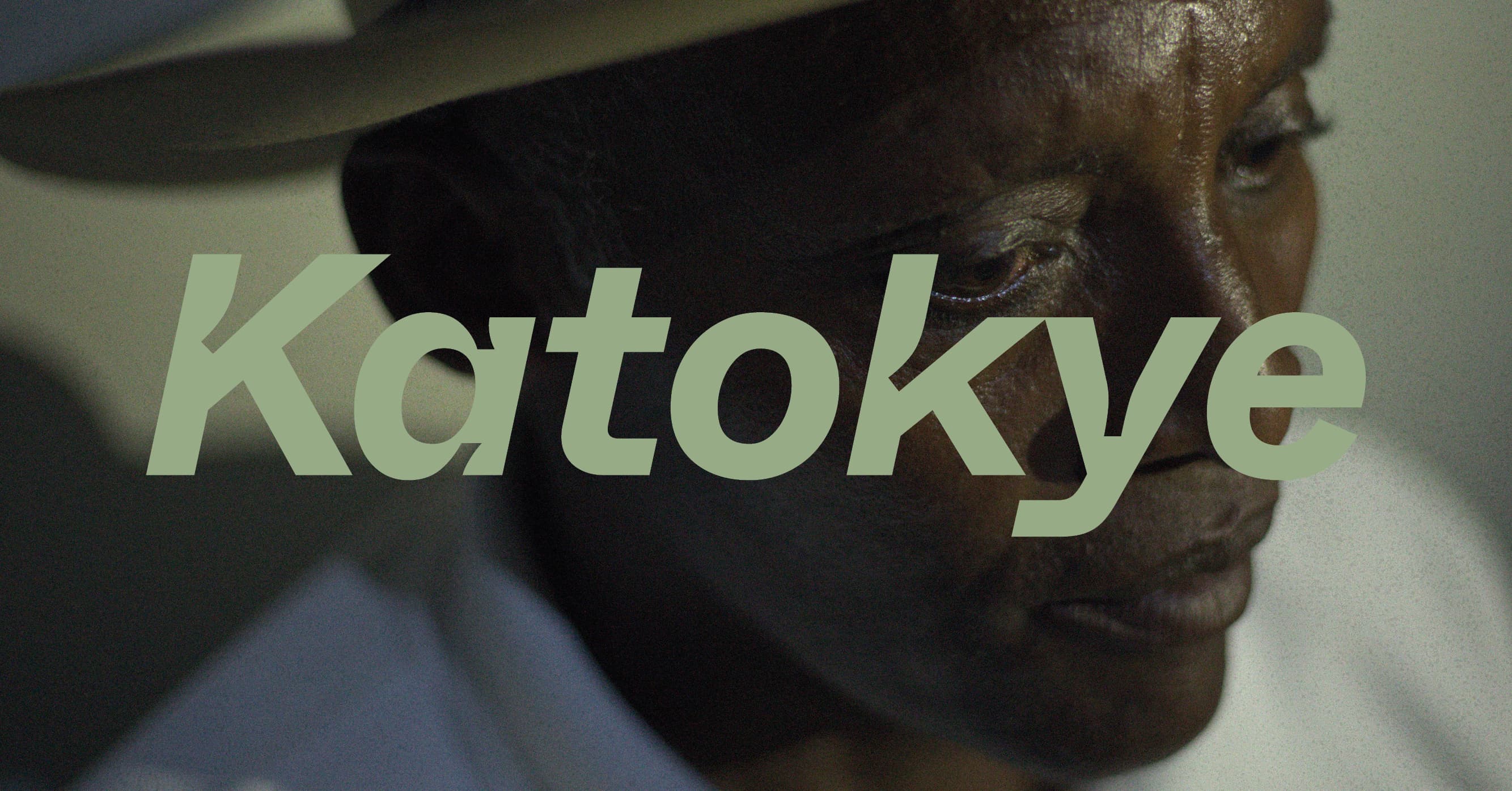 A person wearing a hat is partially visible in the background, with the word "Katokye" overlaid in large green letters.